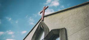 cross at top of church roof with sky in background