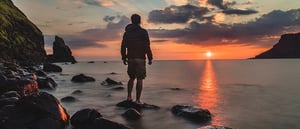 young man standing on shore looking at sunset